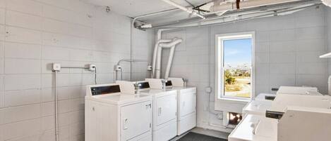 A laundry room with multiple washing machines, a window with a view, and visible plumbing.