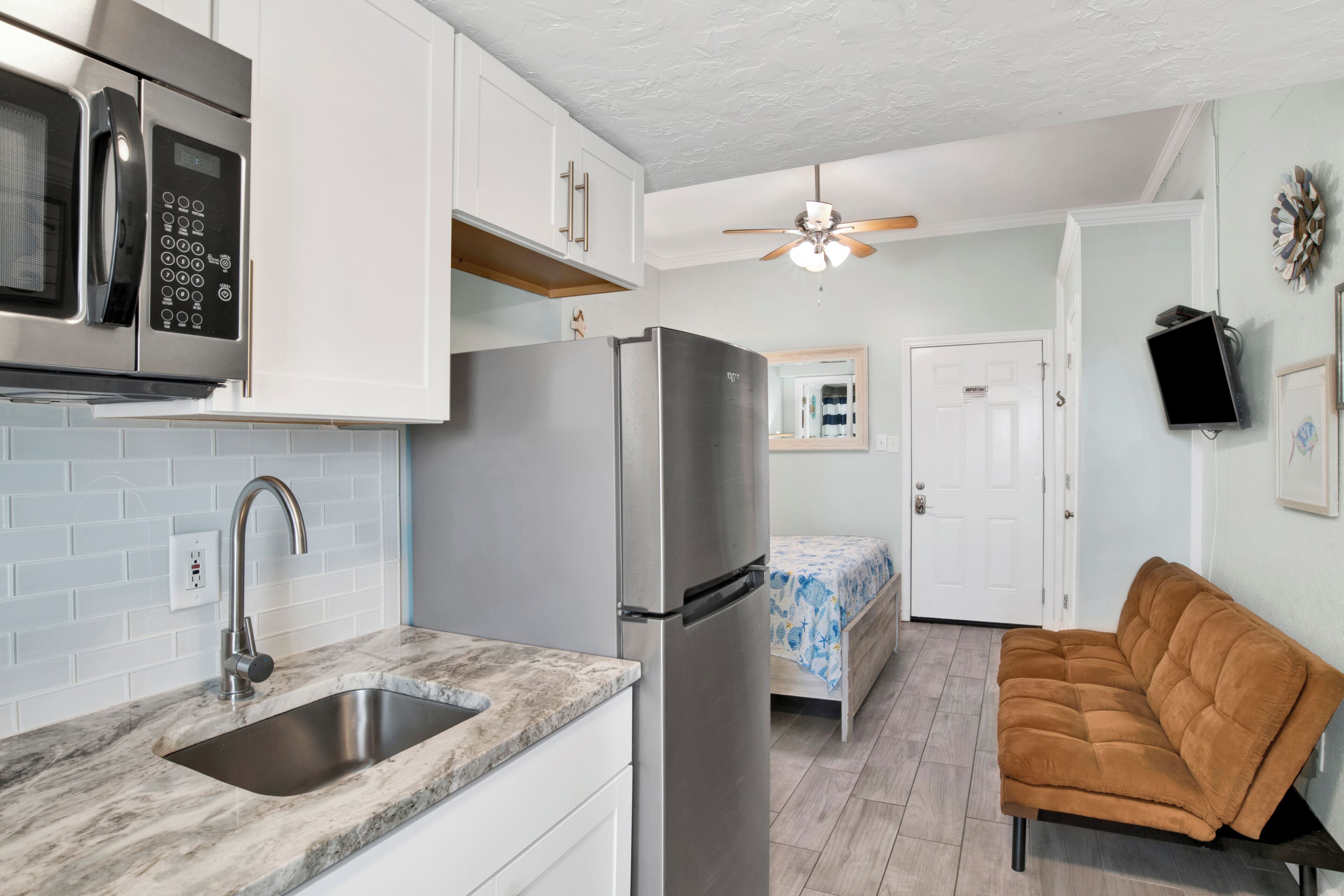 A compact kitchen with white cabinets, a stainless steel refrigerator, and a built-in microwave.
