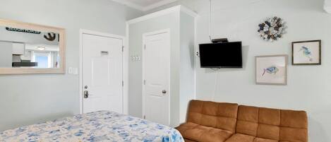 Un dormitorio con una cama, un sofá marrón, una televisión y un televisor de pared.