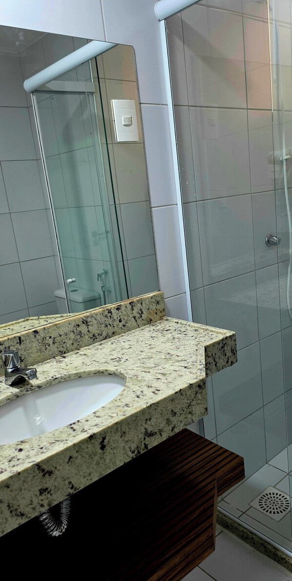 A bathroom with a granite countertop sink, a mirror, and a glass shower enclosure.
