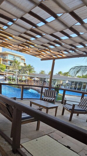 A poolside area with wooden pergolas, lounge chairs, and a view of a building in the background.