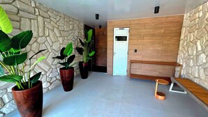 A modern interior with a stone wall, a wooden panel wall, and a white door. There are potted plants and a small wooden bench.