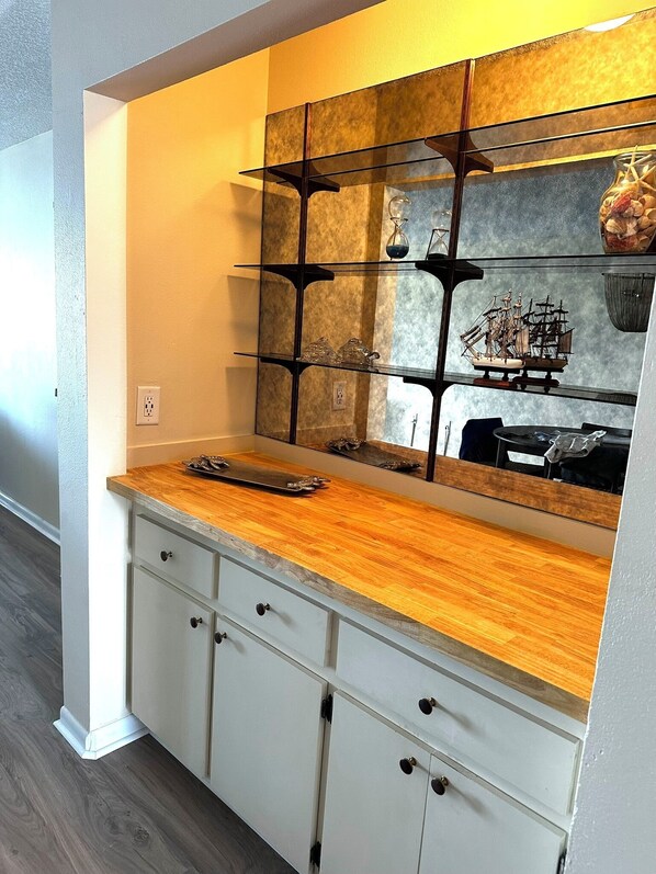 A kitchen with a wooden countertop, white cabinets, and a large mirror with a ship model.