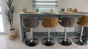 A kitchen with a central island, four bar stools, a potted plant, and a window with blinds. - Vieques Beach Home, Boho style, within walking distance to beach and a King Bed (Florida)