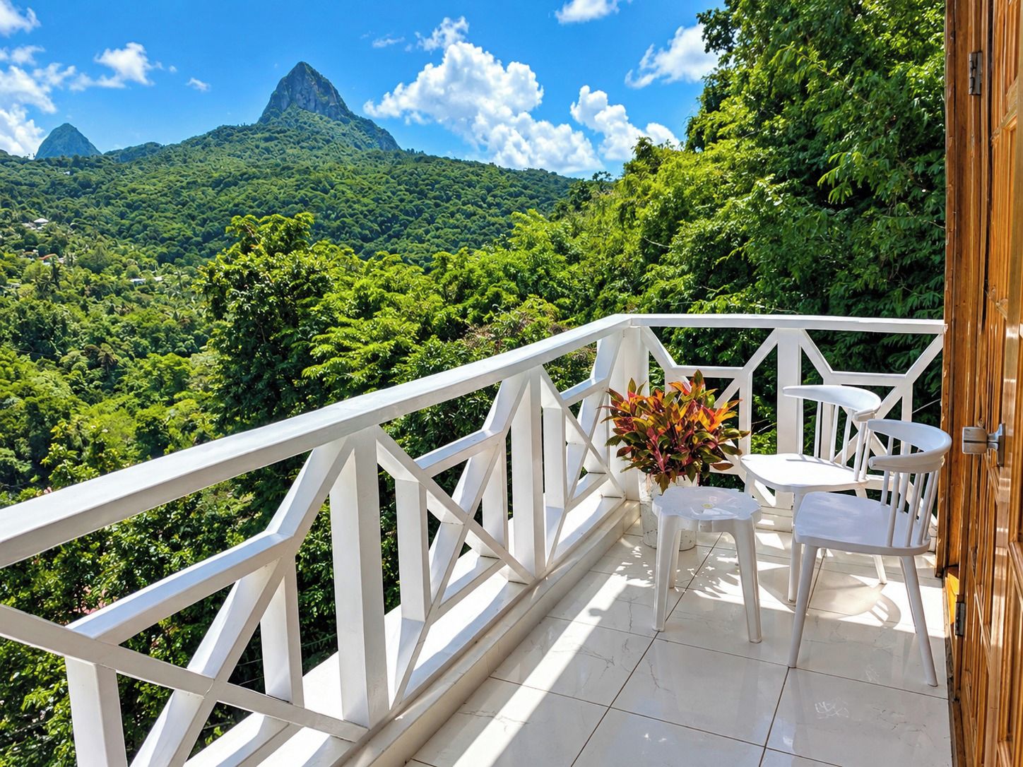 Ein Balkon mit weißer Reling, einem kleinen Tisch und zwei Stühlen mit Blick auf eine üppige grüne Landschaft und einen Berg in der Ferne.