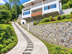 Un edificio moderno de dos pisos con un muro de contención de piedra y un sendero curvo que conduce a la entrada.