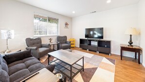 Uma sala de estar moderna com um sofá, poltronas, uma mesa de centro, uma televisão e um abajur.