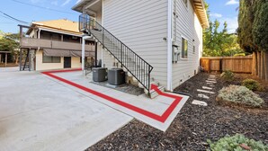 Uma casa de dois andares com uma escadaria visível para o segundo andar, um caminho vermelho e aparelhos de ar condicionado externos.