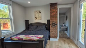 A bedroom with a dark wooden bed, a quilt, a brick accent wall, and a view of the outdoors through a window. - Quidi Vidi Escape (St. John's)