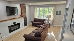 A modern living room with a fireplace, leather sofas, a flat-screen TV, and a large window with curtains. - Quidi Vidi Escape (St. John's)
