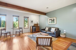 Un salón espacioso con suelo de madera, un sofá, dos sillones, una mesa de centro y un pequeño armario.