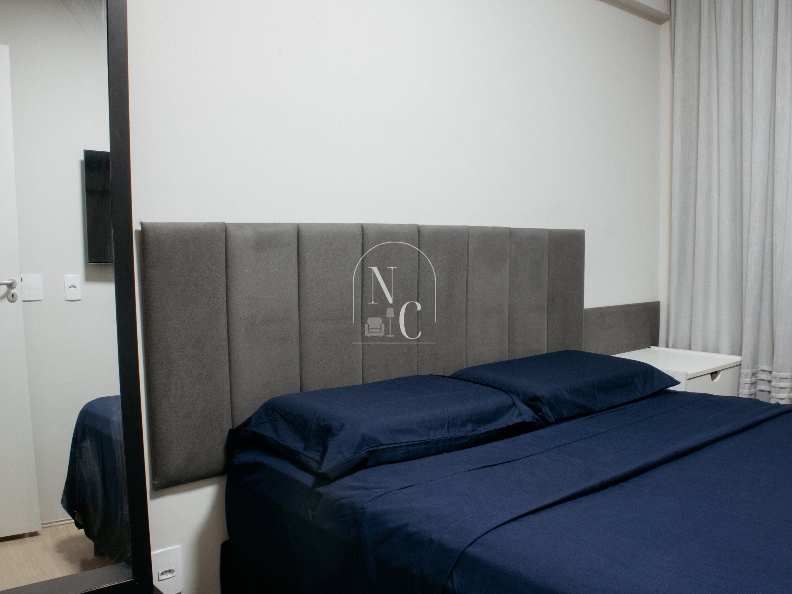 A hotel room with a bed, a small bedside table, a flat-screen TV mounted on the wall, and a window with curtains.