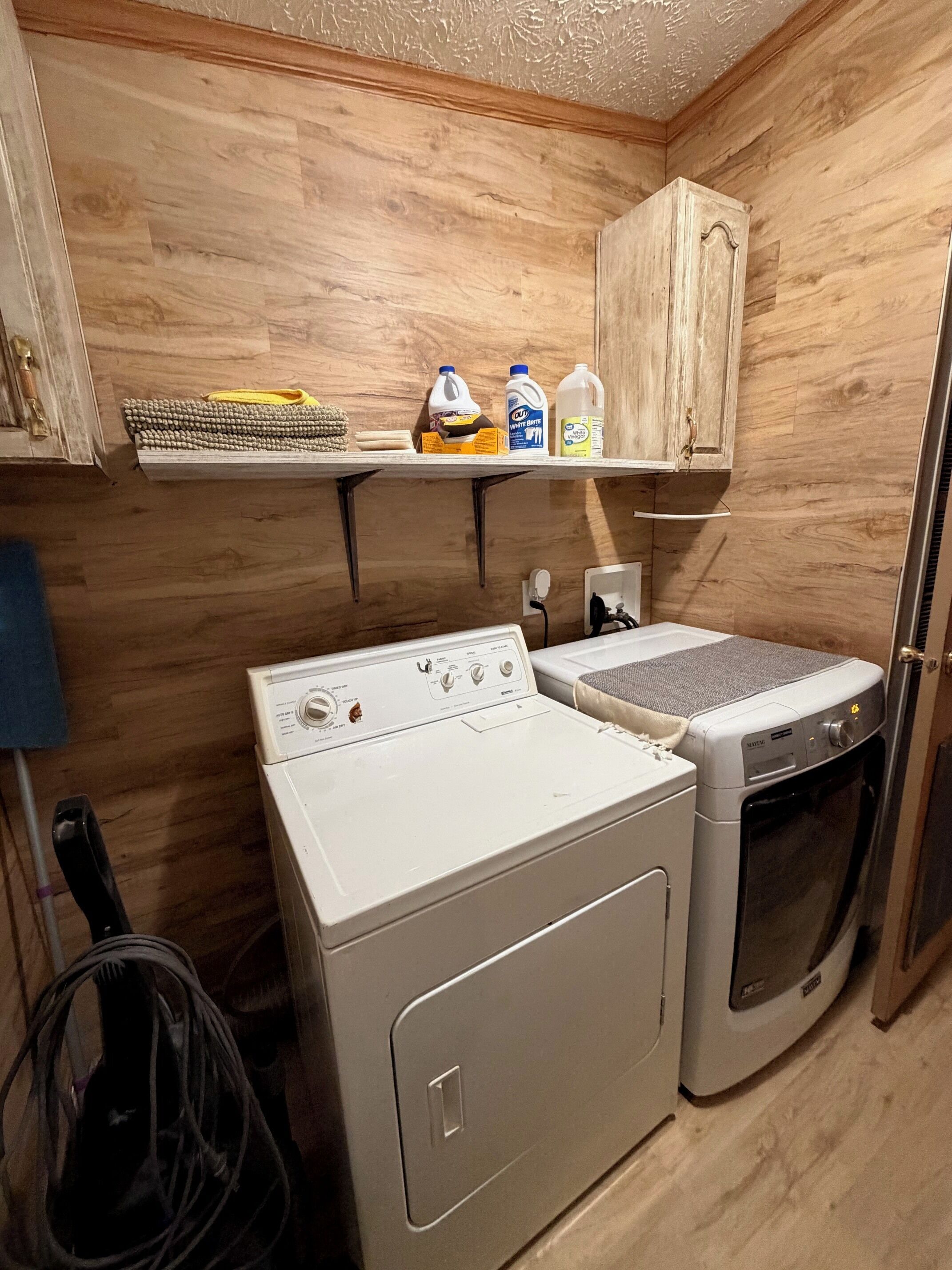 A laundry room with a washing machine, dryer, and shelves above containing cleaning supplies.