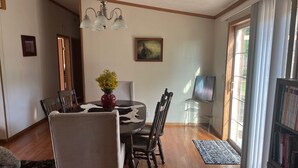 Un coin repas avec une table ronde, des chaises, un vase de fleurs, un lustre, un tableau et une bibliothèque.