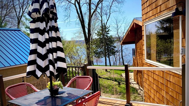 Una terraza de madera con una mesa y sillas, con vista a un cuerpo de agua y árboles.
