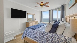 Un dormitorio con cama, ventilador de techo, televisor, cómoda y ventana con vistas.