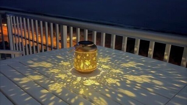 Una mesa blanca al aire libre con un farol decorativo en el centro, rodeada por una barandilla.