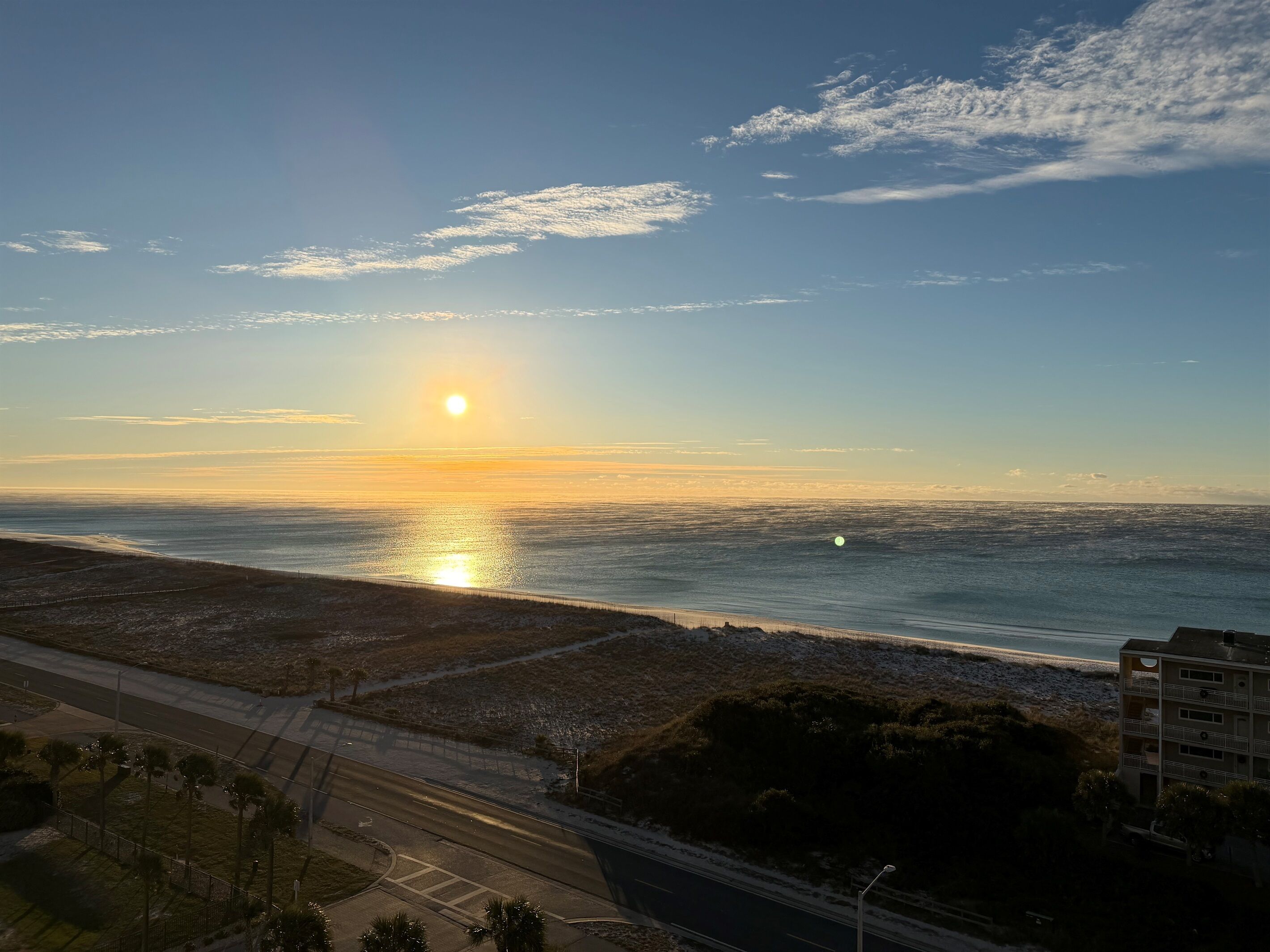 Una carretera costera con una playa al fondo, cielo despejado y un edificio de varios pisos.