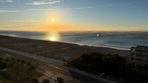 Una carretera costera con una playa al fondo, cielo despejado y un edificio de varios pisos.