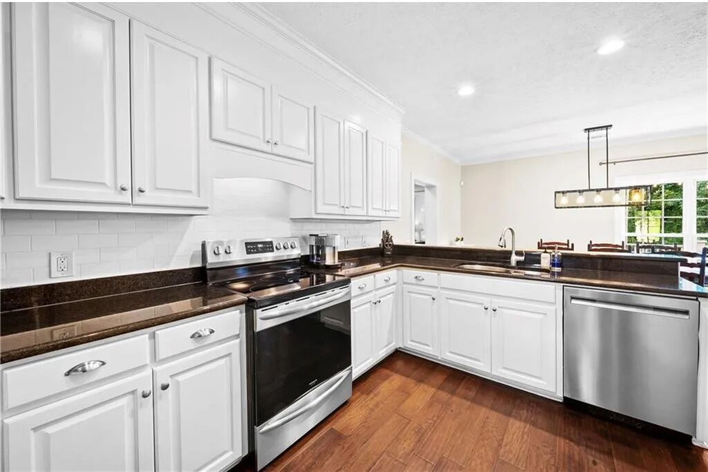 A modern kitchen with white cabinetry, a stainless steel dishwasher, and a dark brown countertop.