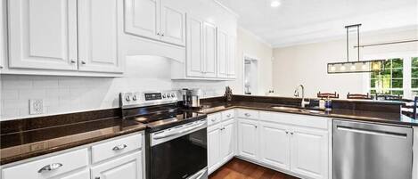 A modern kitchen with white cabinetry, a stainless steel dishwasher, and a dark brown countertop.