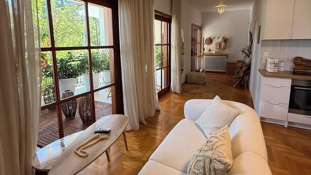 A spacious living area with a large sofa, a wooden coffee table, and a view through large windows.