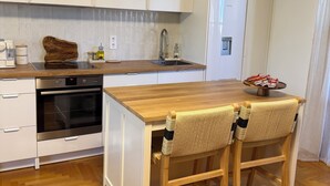 A modern kitchen with white cabinetry, a built-in oven, a sink, and a wooden dining table with two chairs.