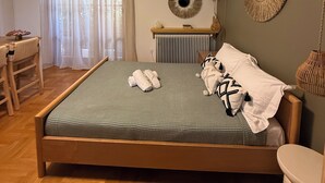 A bedroom with a bed, a bedside table, a radiator, a window with curtains, and a wall-mounted mirror.