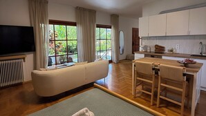 A modern living room with a sofa, a dining table with chairs, a TV, and a kitchen area.