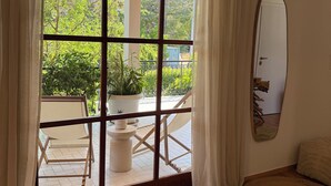 A room with a large sliding glass door leading to an outdoor area with a white chair, a small table, and a potted plant.