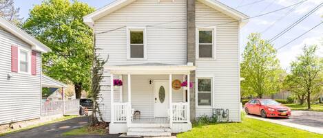A two-story house with a front porch, a chimney, and a car parked in the driveway.