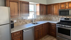 A kitchen with wooden cabinets, a stainless steel refrigerator, a microwave, a stove, and a dishwasher. - Spacious Long Beach home, steps to beach & train (Long Beach)