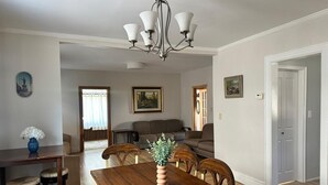 A dining area with a wooden table, chairs, and a chandelier. There is a sofa and a painting on the wall. - Spacious Long Beach home, steps to beach & train (Long Beach)