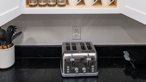 A kitchen with a built-in cabinet containing glassware and mugs, a kettle, and a toaster on the countertop.