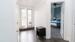 A hallway leading to a bedroom with a bed, a ceiling fan, and a small table.