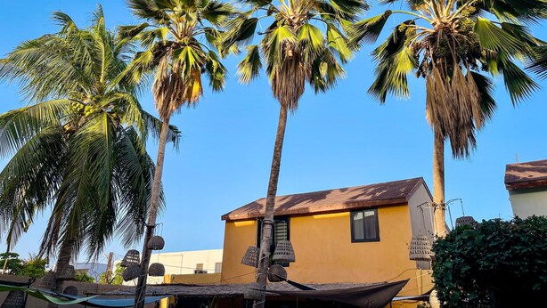 A yellow building with a thatched roof and a hammock.