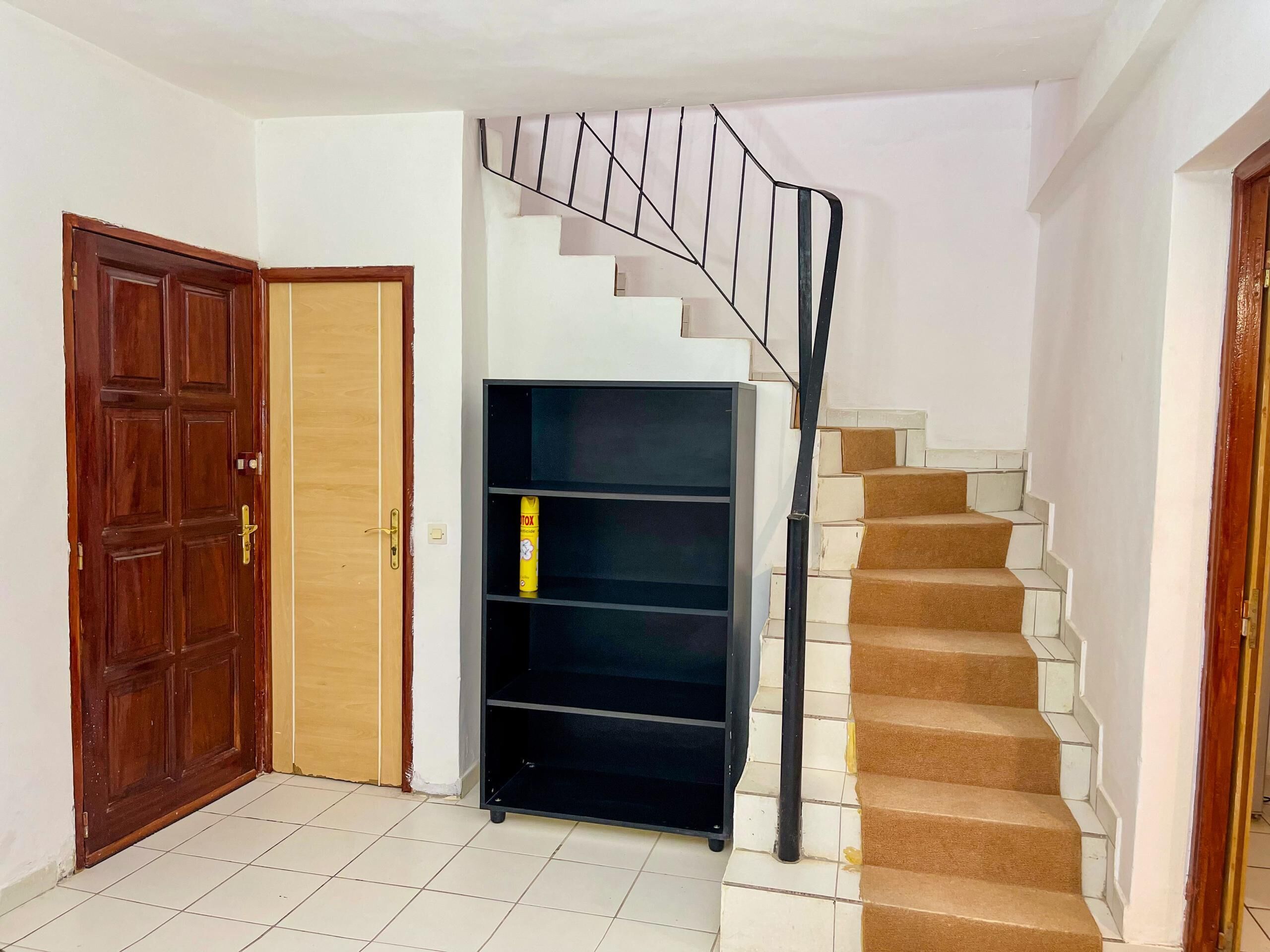 A staircase with a metal railing, a wooden door, and a black shelving unit with a yellow object on the lower shelf.
