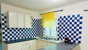 A kitchen with white cabinets, blue and white checkered backsplash, a granite countertop, and a yellow curtain.