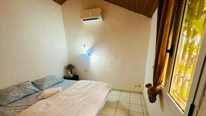 A bedroom with a bed, a nightstand, a wall-mounted air conditioner, and a window with curtains.