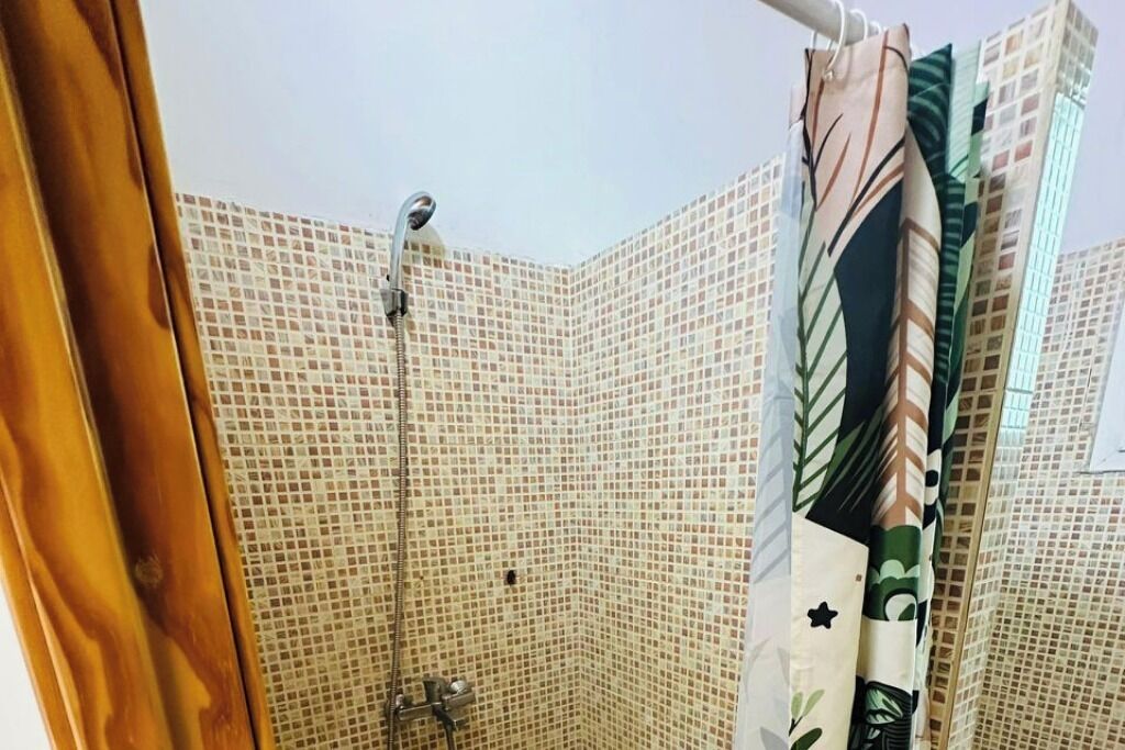 A corner bathroom with mosaic tile walls, a shower, and a curtain with a leaf pattern.
