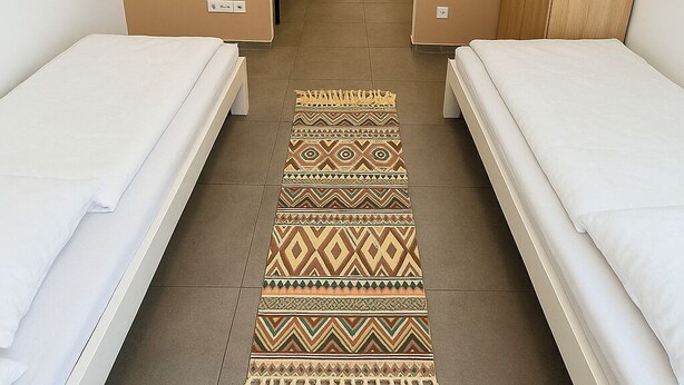 A hotel room with two single beds, a TV mounted on the wall, a wooden wardrobe, and a patterned rug on the floor. - City apartment no. 6 with comfort (Pforzheim)