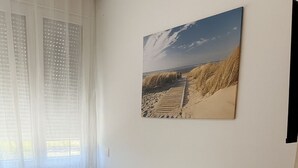 A minimalist bedroom with a single bed, a bedside table, a lamp, and a large landscape painting on the wall. - City apartment no. 6 with comfort (Pforzheim)