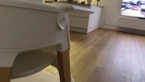 Una sala de estar con un sillón blanco, piso de madera y un televisor que muestra una escena de aeropuerto.