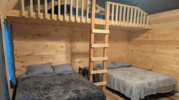 Una cabaña de madera con dos literas, una escalera y una mesita.