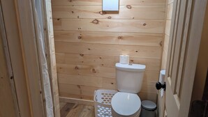 Un baño pequeño con paneles de madera, un inodoro, un cesto de basura y una cesta de ropa.
