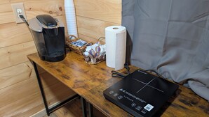 Una mesa de madera con una cafetera, una cesta de revistas, un rollo de toallas de papel y un dispositivo electrónico negro.