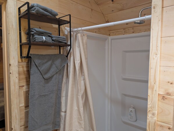 Ett badrum i en stuga med träpanel, ett duschdraperi, en hylla med hopvikta handdukar och en flaska Dove-tvål.