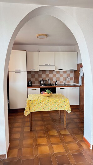 Une cuisine avec un sol carrelé, une table recouverte d’une nappe à pois et un réfrigérateur.