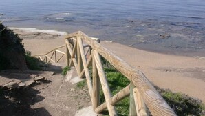 Un escalier en bois descend vers une plage de sable, avec l’océan en toile de fond.