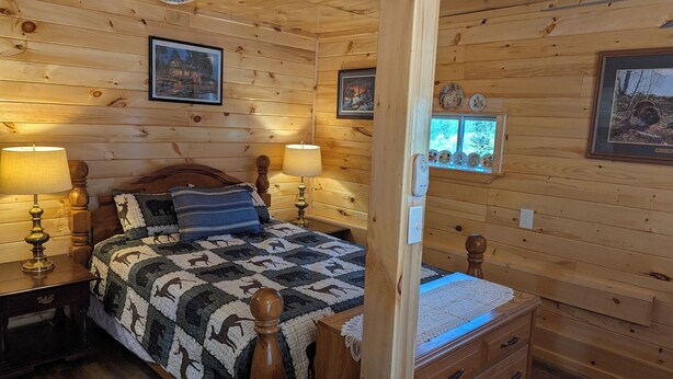 Um quarto de cabana de madeira aconchegante, com cama, duas luminárias de cabeceira, mesa de cabeceira, cômoda e quadros nas paredes.